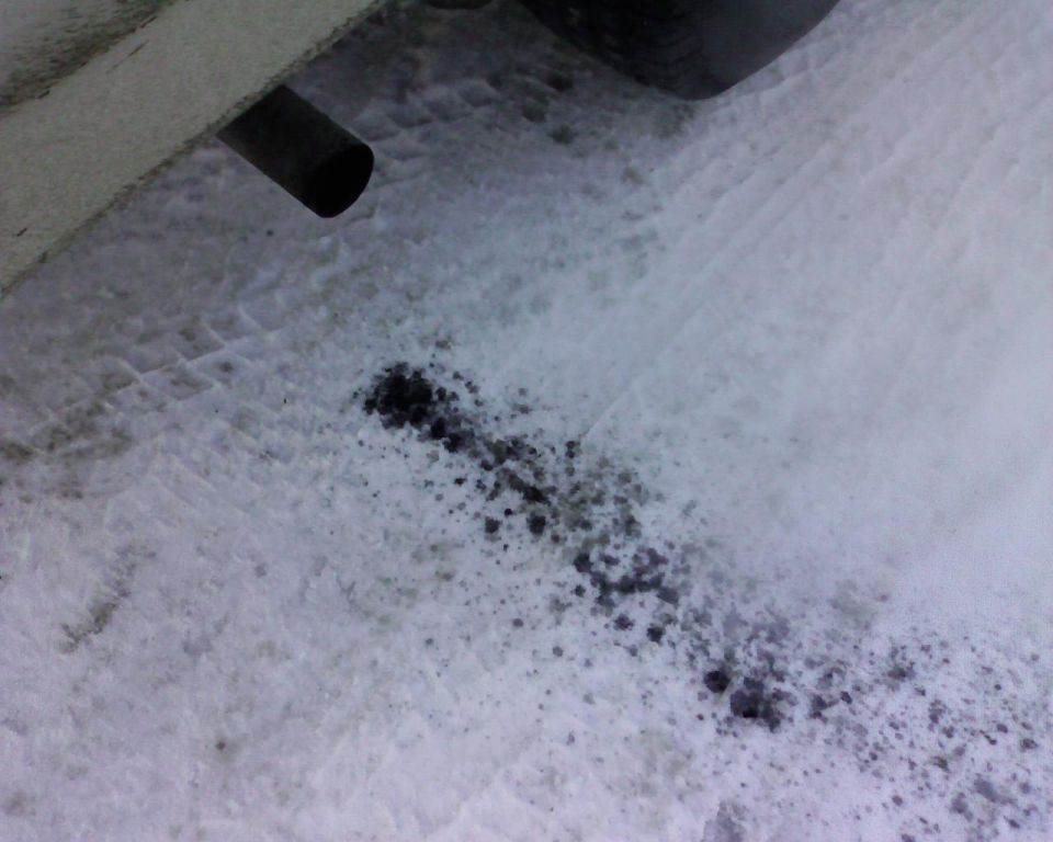 Exhaust pipe on a vehicle, dripping dark liquid onto snow with tire tracks