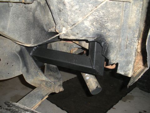1979 Ford Bronco - Interior tub shot of a fabricated black square-tube cage leg running down to a welded mount plate against the stripped, dirt-caked wheelhou…