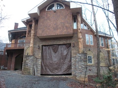 1979 Ford Bronco - Exterior of a wooded hillside house with cedar shake and stone siding, log posts and an oversized garage bay opening covered by a brown tar…