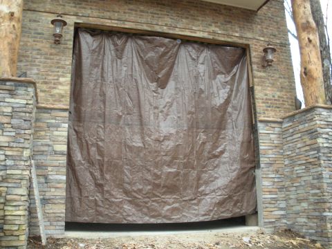 1979 Ford Bronco - A tall garage bay opening in a brick and stacked-stone wall, temporarily closed off with a brown tarp hung from the header, flanked by two…