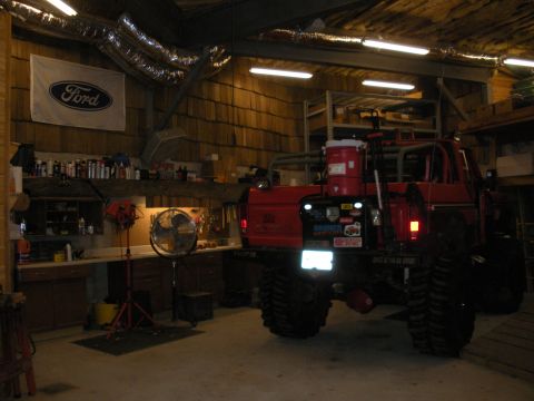 1979 Ford Bronco - Rear three-quarter view of a heavily lifted red Ford Bronco parked in a wood-lined shop with its reverse lights on, showing sticker-covered…