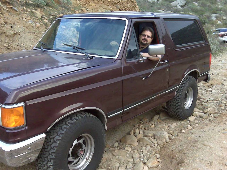 Maroon Ford Bronco with a man driving, on a rocky, off-road trail