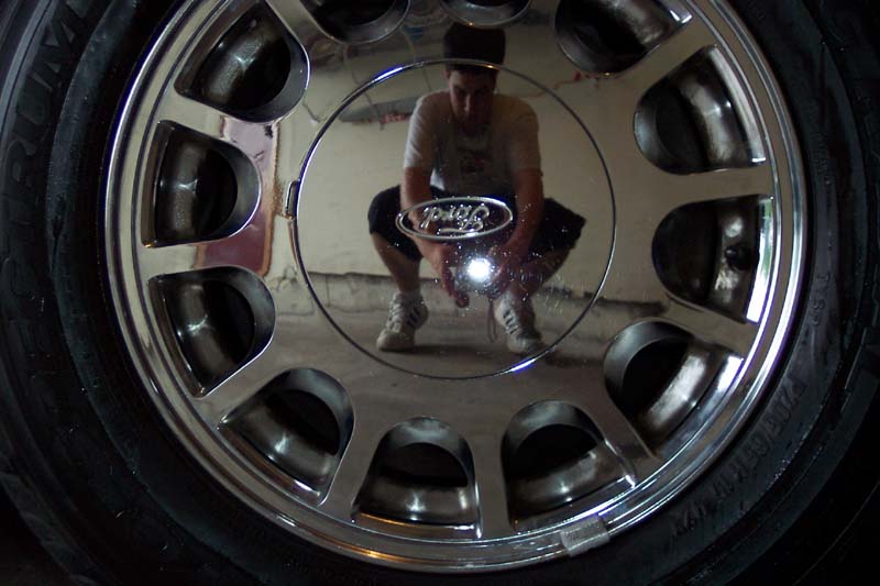 Chrome 10-spoke Ford alloy wheel with the photographer's reflection visible in the center cap