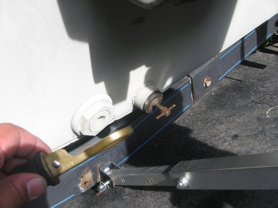 Hand holding a brass link arm against a black boat transom with blue pinstripe