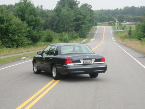 1998 Ford Crown Victoria - A dark 1998 Ford Crown Victoria is seen from the rear driving on a two-lane road.