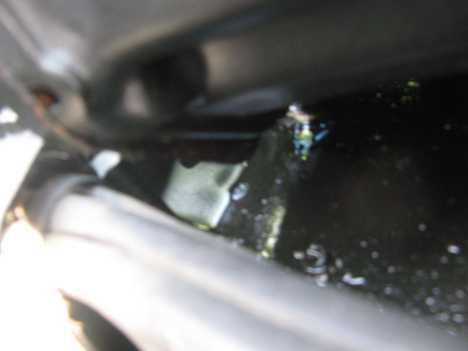 Blurred close-up of a bracket, bolt and gray tube inside a dark painted cavity
