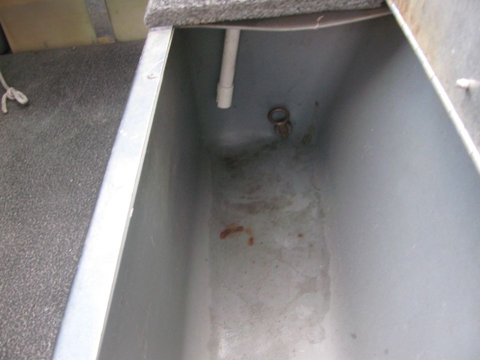 Open gray aluminum livewell in a boat deck with white PVC standpipe and brass drain