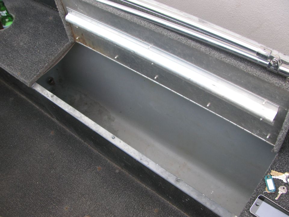 Open bare aluminum rod locker in a boat's gray carpeted deck with piano-hinge lid