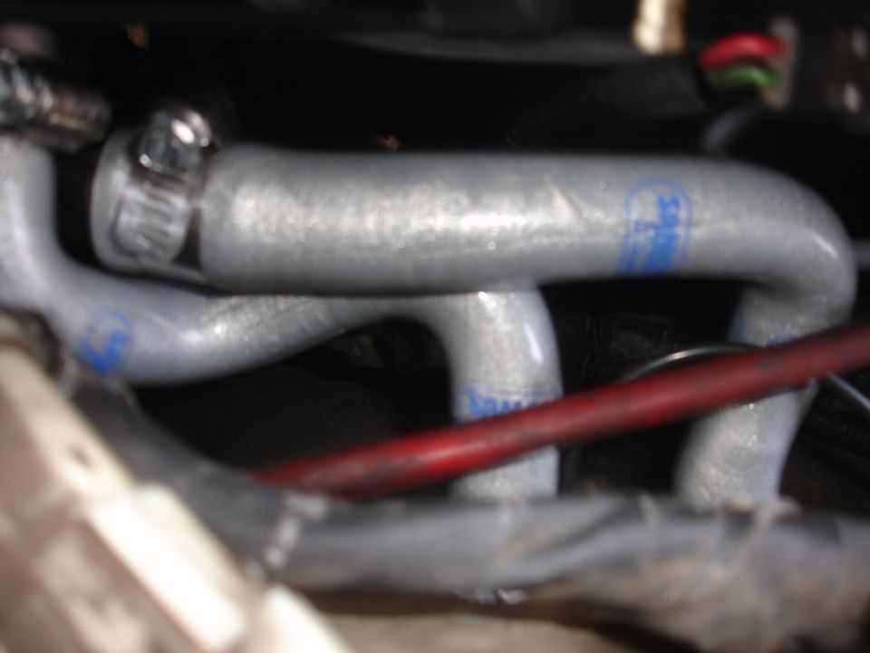 Close-up of silver engine hoses with blue markings and a red wire