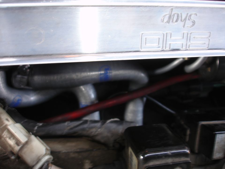Engine bay with metal cover embossed with 'dovs OHS' and gray hoses