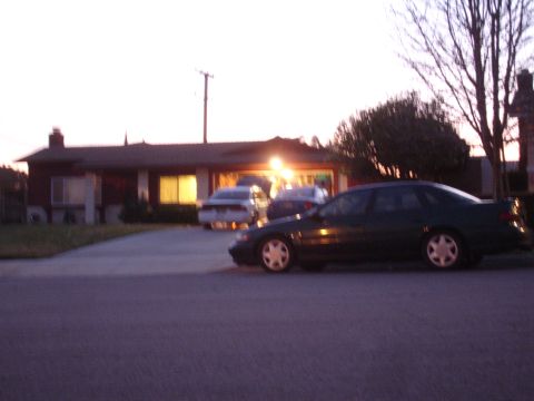 1993 Ford Taurus - A dark sedan is parked in front of a house at dusk, with other vehicles visible in the driveway.