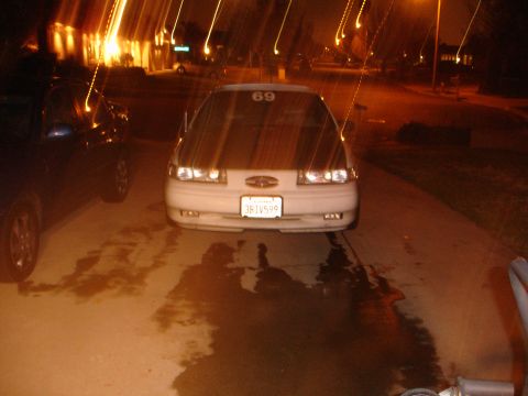 1993 Ford Taurus - A white sedan with racing stripes on the hood is parked in a driveway at night.