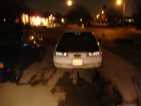 1993 Ford Taurus - A 1993 Ford Taurus with a black hood is parked at night next to another vehicle.