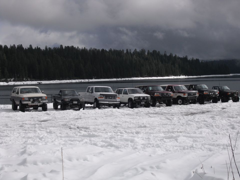 Line of 1991 Ford Broncos and other SUVs parked in the snow near a lake