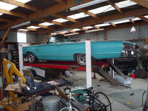 1969 Lincoln Continental - A turquoise convertible is raised on a car lift inside a workshop, revealing its side profile.