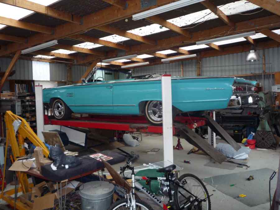 Turquoise convertible on a red car lift, viewed from the side in a garage