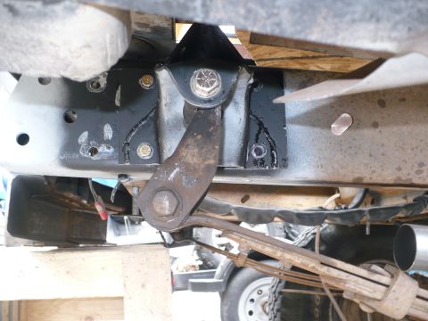 1979 Ford Bronco - Underbody view of a truck frame rail showing a fresh black-painted steering box mounting plate welded and bolted to the frame, with a rusty…