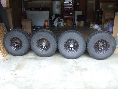 1996 Ford Bronco - Four off-road tires and wheels are displayed in a garage setting.