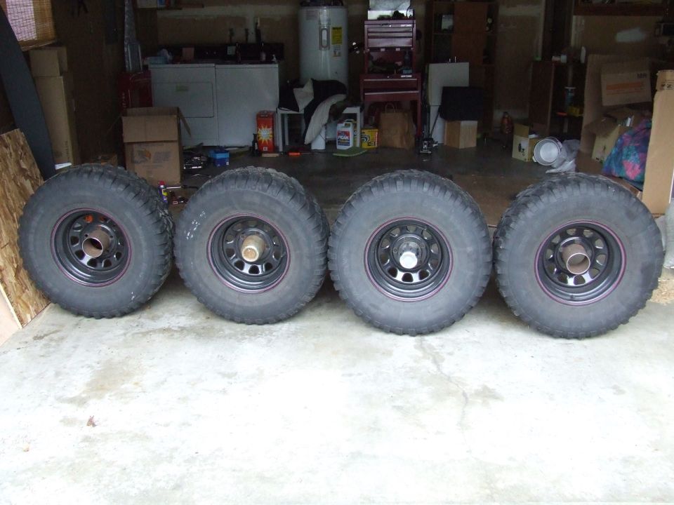 four off-road tires and wheels lined up in a garage