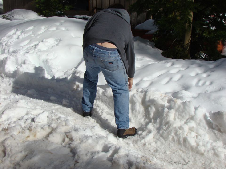 Person bending over in snow, wearing jeans and a hoodie