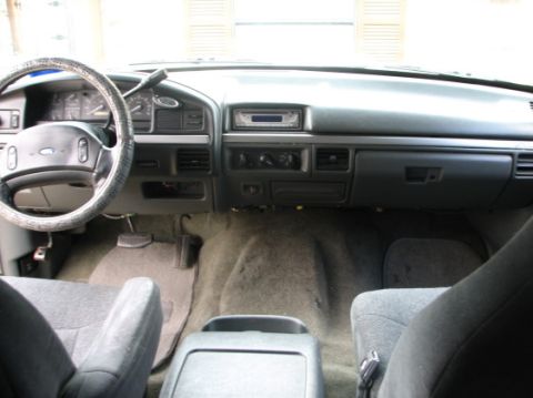 1992 Ford Bronco - The dashboard and interior of a Ford truck, an aftermarket radio and a worn steering wheel cover.