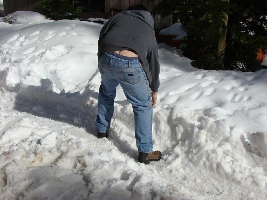 Person bent over in snow, wearing jeans and a grey hoodie