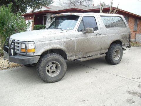 1992 Ford Bronco - A muddy 1992 Ford Bronco is parked in front of a house.