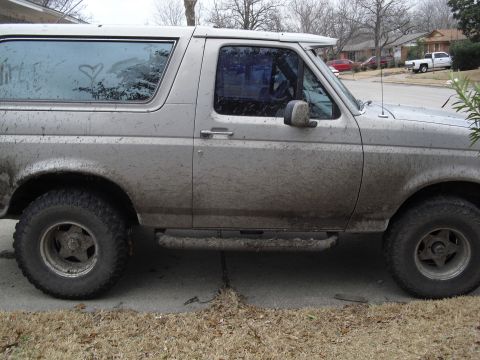 1992 Ford Bronco - Side view of a dirty 1992 Ford Bronco parked on a residential street.