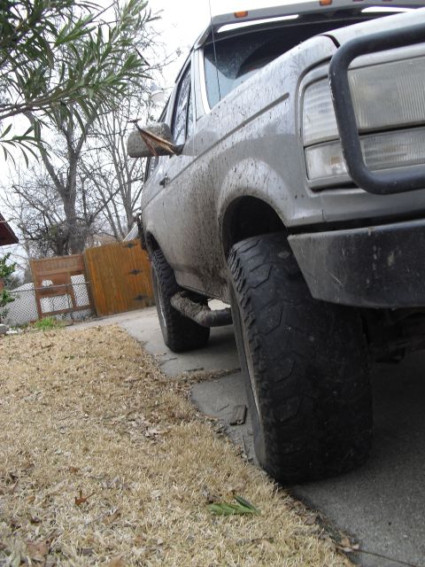 1992 Ford Bronco - This 1992 Ford Bronco is captured from a 3/4 front angle, highlighting its off-road tires and the mud splattered across its silver body.