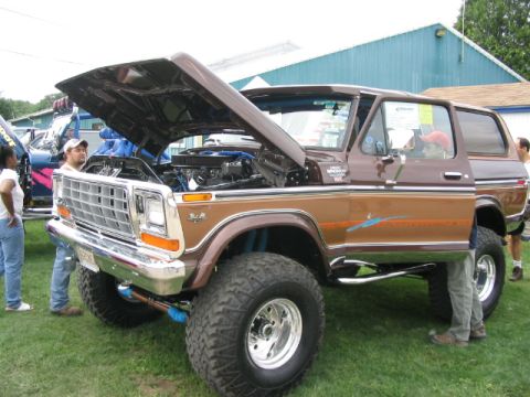 1986 Ford Bronco - A lifted brown Ford Bronco is displayed with its hood open at an outdoor event.