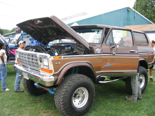 Brown two-tone lifted Ford Bronco at a car show with hood open showing blue V8