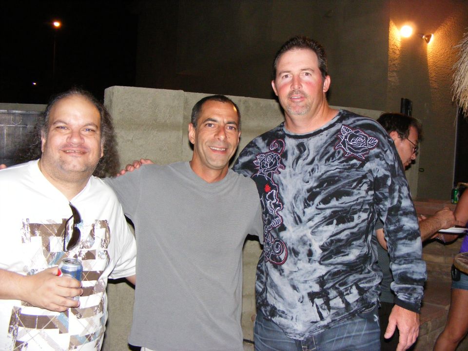 Three men and a woman stand together outdoors at night, with a concrete wall behind them