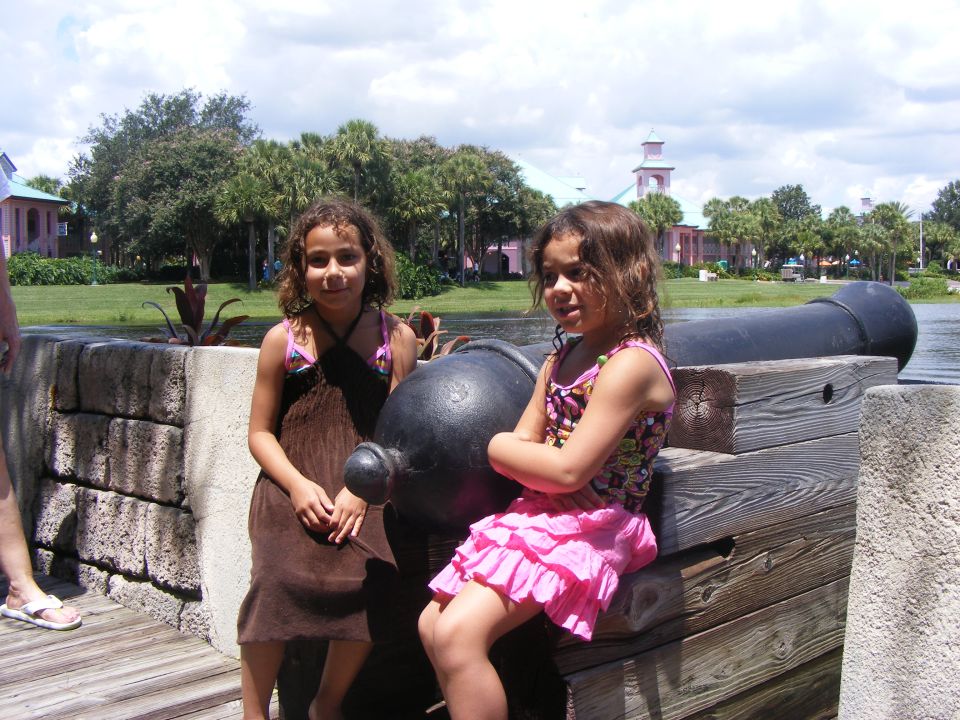 Two girls sit on a wooden platform next to a large cannon
