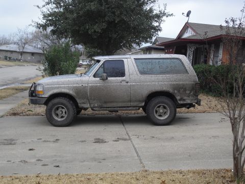 1992 Ford Bronco - A muddy 1992 Ford Bronco is parked on a residential street.