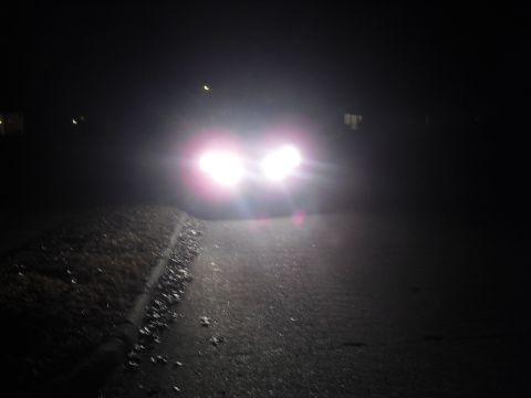 1992 Ford Bronco - Headlights of an unidentified vehicle shine brightly on a dark, leaf-strewn road.