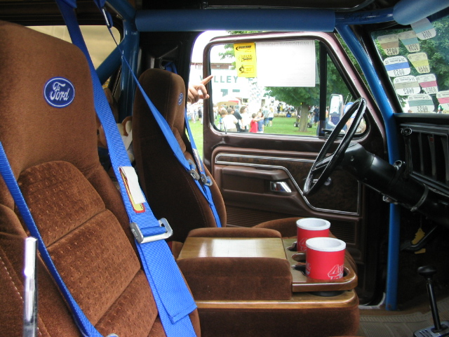 1986 Ford Bronco interior with brown seats, blue harnesses, and a roll cage