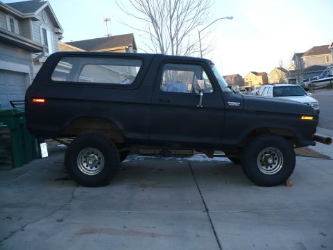1979 Ford Bronco - Passenger-side profile of a lifted flat-black Ford Bronco Custom two-door SUV with removable hardtop, "BRONCO CUSTOM" fender badge, amber s…