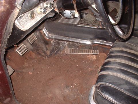 1963 Ford Galaxie - The interior floor of a 1963 Ford Galaxie shows pedals, a vent, and the edge of a seat, all covered in dirt.