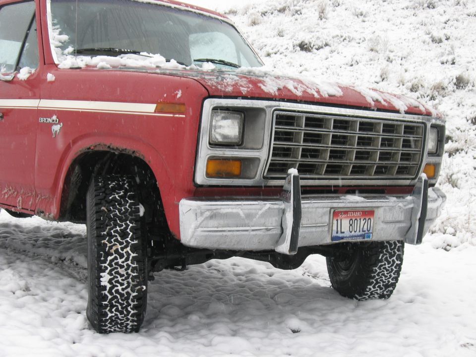 Red Ford Bronco with off-road tires in snow. License plate reads IL 80120