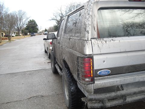 1992 Ford Bronco - This heavily mud-splattered 1992 Ford Bronco is seen from the rear, with its distinctive taillights and Ford badging visible.