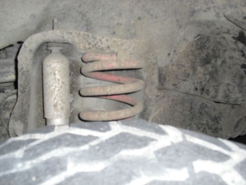 1992 Ford Bronco - Close-up view of a vehicle's front suspension coil spring and shock absorber, showing signs of wear and tear.