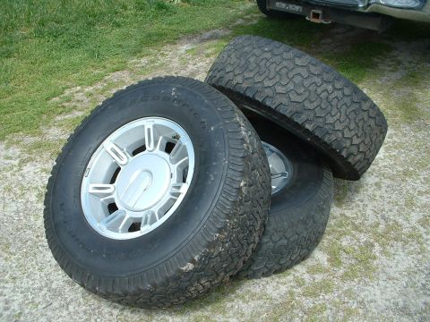 1994 GMC Suburban - Three tires and rims are stacked on the ground, with a vehicle hitch visible in the background.