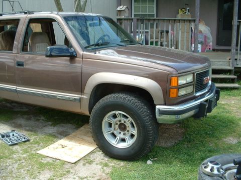 1994 GMC Suburban - This 1994 GMC Suburban is parked on a grassy area with a toolbox and plywood in front of the wheel.