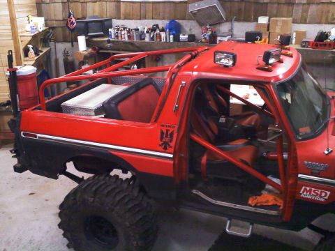 1979 Ford Bronco - Side view of a red topless Ford Bronco Ranger trail rig inside a workshop, with a full red exterior/interior roll cage, red bucket seats wi…