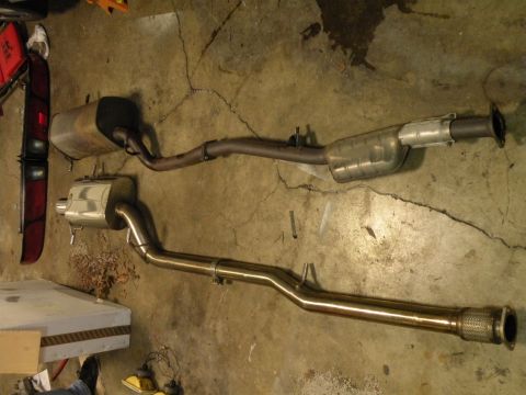 1998 Subaru Legacy - Two exhaust systems are laid out on a concrete floor, one appears to be a performance upgrade with its polished stainless steel finish.