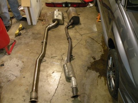 1998 Subaru Legacy - Comparison of a new exhaust system with an older, corroded one, with a vehicle partially visible.