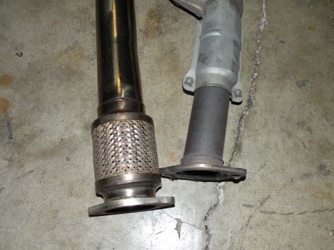 1998 Subaru Legacy - Close-up of two exhaust pipes, one a flexible braided section, on a concrete surface.