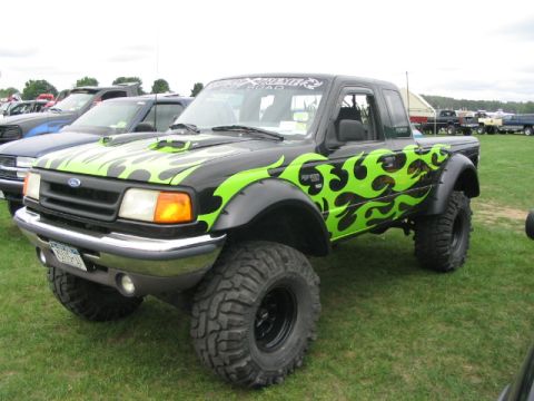 1986 Ford Bronco - A modified Ford Ranger pickup truck with custom flame decals sits on a grassy field at an outdoor event.