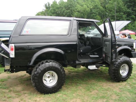 1986 Ford Bronco - A modified black Ford Bronco is displayed at an outdoor event with its doors open.