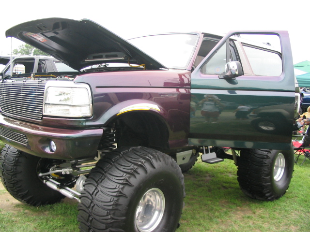 Lifted Ford truck with purple and green paint, hood open, and large tires